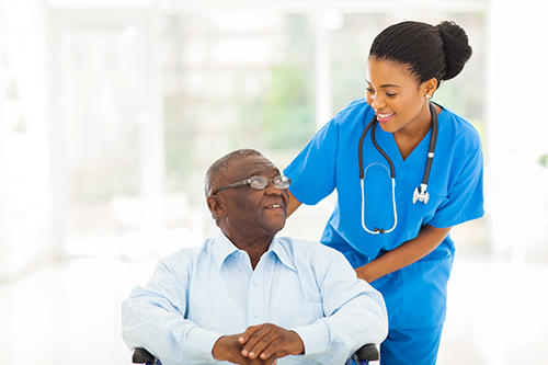 African american nurse in blue scrubs smiling at elderly man in wheelchair next to her