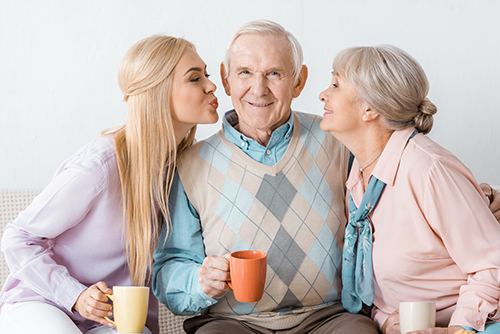 Grandfather in between his wife and granddaughter kissing his cheeks